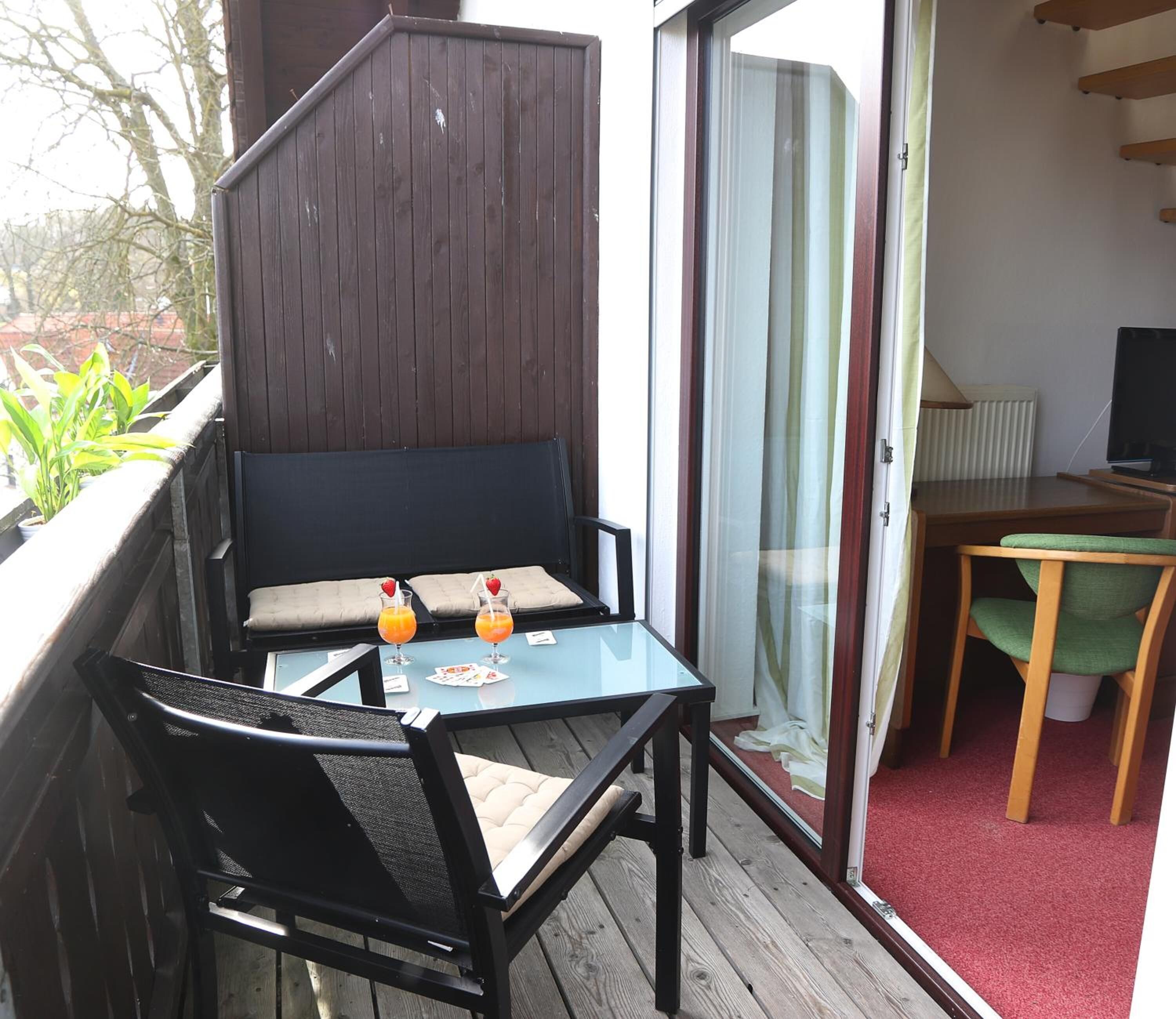 A balcony with a wooden deck, a glass table with two chairs, and a small table with a TV and lamp.