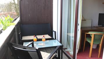 A balcony with a wooden deck, a glass table with two chairs, and a small table with a TV and lamp.