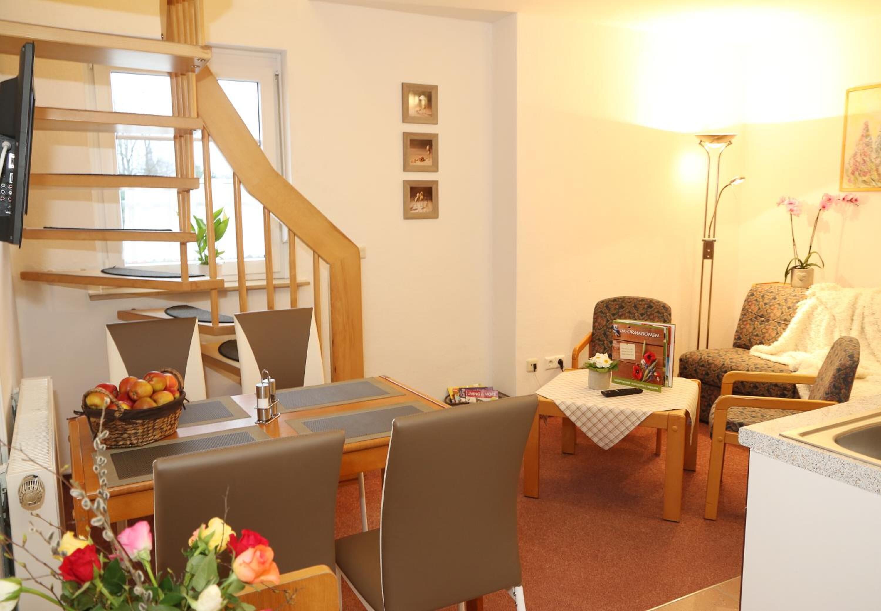 A cozy living room with a dining area, a staircase, and a kitchen.