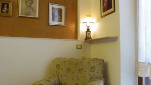 A living room with a patterned armchair, a wall-mounted lamp, and framed artwork. - B&B Al Ponte Vecchio (Perugia)