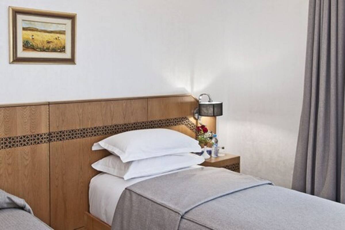 A hotel room with a wooden headboard, a bedside table with a lamp, and a framed picture on the wall.