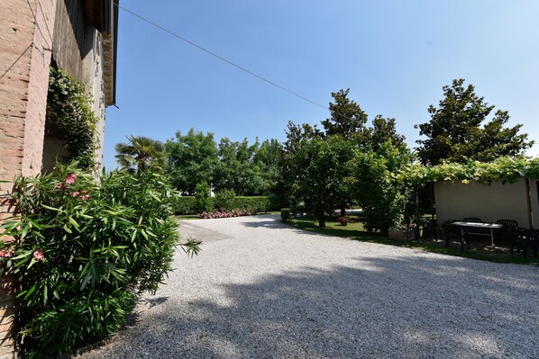 A gravel driveway leading to a building with a brick facade, surrounded by lush greenery and trees. - B&B Kiwi (Agugliaro)