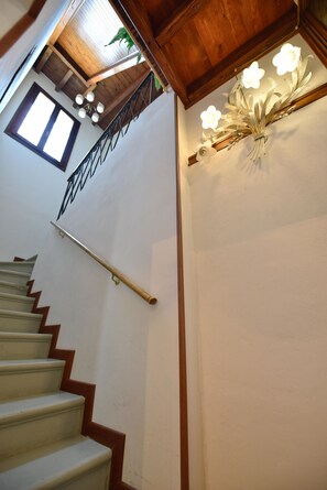 A staircase with wooden railings and a handrail, leading to a landing with a wall-mounted light fixture. - B&B Kiwi (Agugliaro)