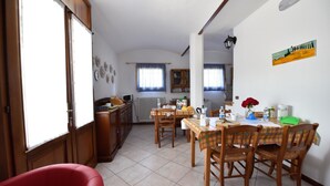 Un coin repas avec une table et des chaises en bois, une chaise rouge, et une cuisine en arrière-plan.