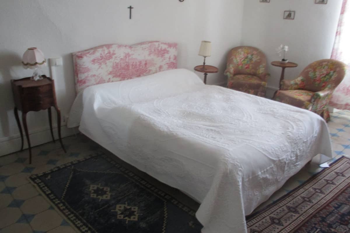 Un dormitorio con cama, mesita de noche, silla, una pequeña mesa y una alfombra.