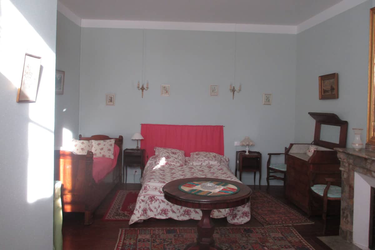 Una habitación con una cama, una pequeña mesa redonda, una silla, una chimenea y un espejo.