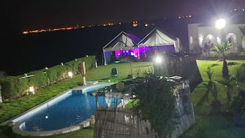A nighttime view of a resort with a swimming pool, two guest cottages, and a large building with illuminated windows.