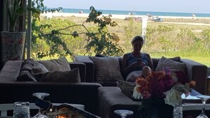 Ein Wohnzimmer mit Blick auf den Strand, eine Couch, ein Tisch mit Blumen und ein Fernseher.