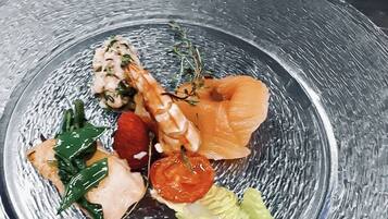 Een bord met diverse soorten eten, waaronder zalm, een tomaat en groenten.