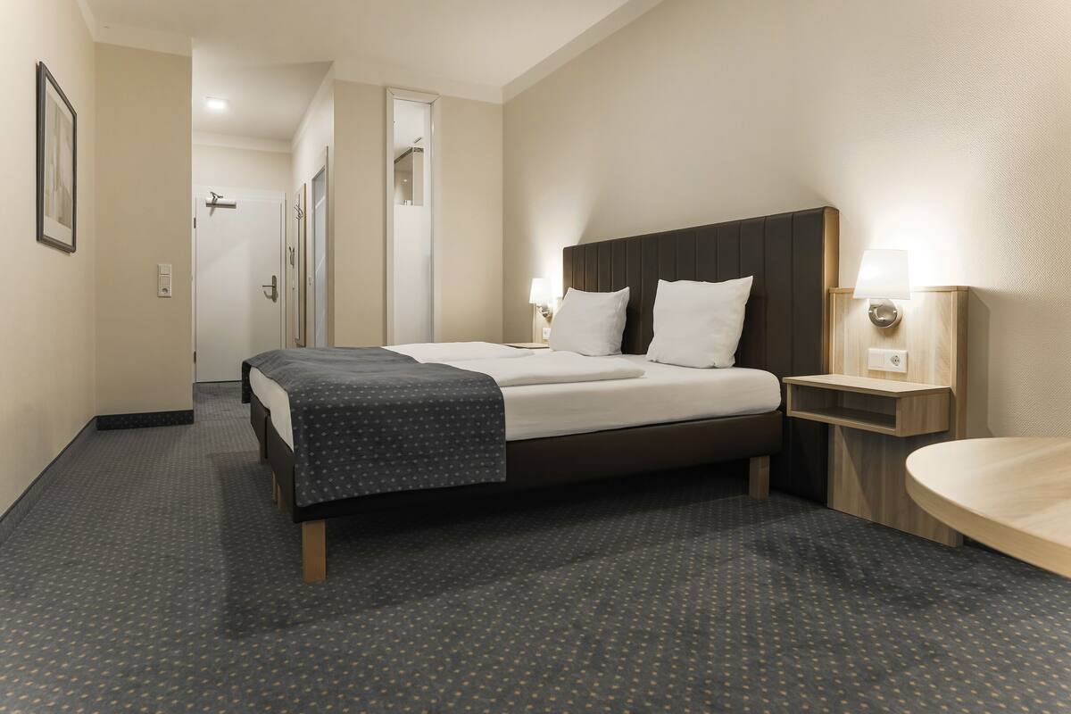 A hotel room with a bed, bedside table, and a bathroom area.