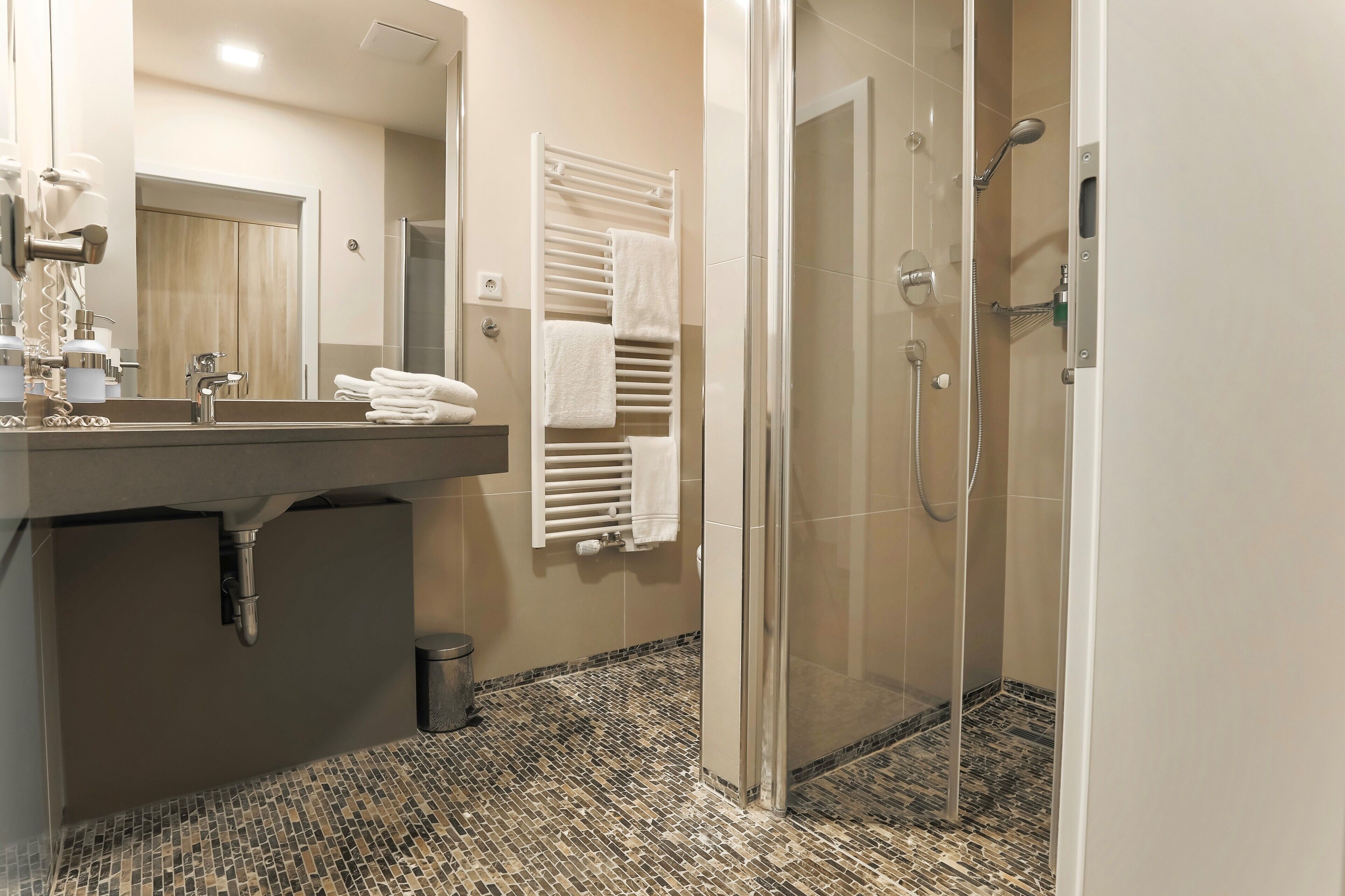 Ein modernes Badezimmer mit einer Glaskabine zur Dusche, einem großen Spiegel und einem Fliesenboden.