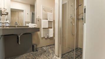 Ein modernes Badezimmer mit einer Glaskabine zur Dusche, einem großen Spiegel und einem Fliesenboden.