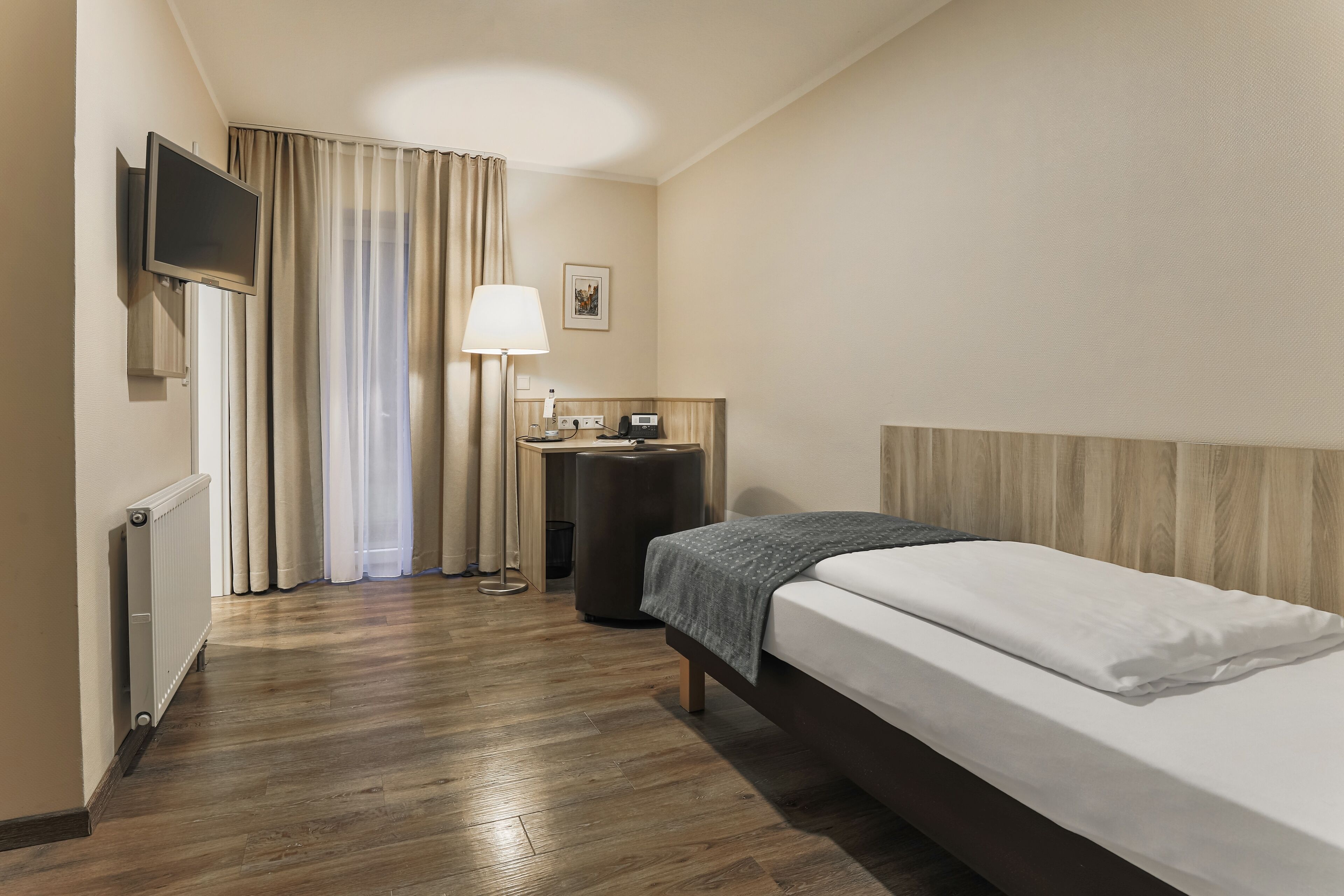 A hotel room with a bed, a desk, a lamp, a TV, and a window with curtains.