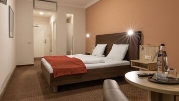 Une chambre d’hôtel avec un lit, une table de chevet avec une bouteille et un verre, une chaise et une petite table avec une télécommande.