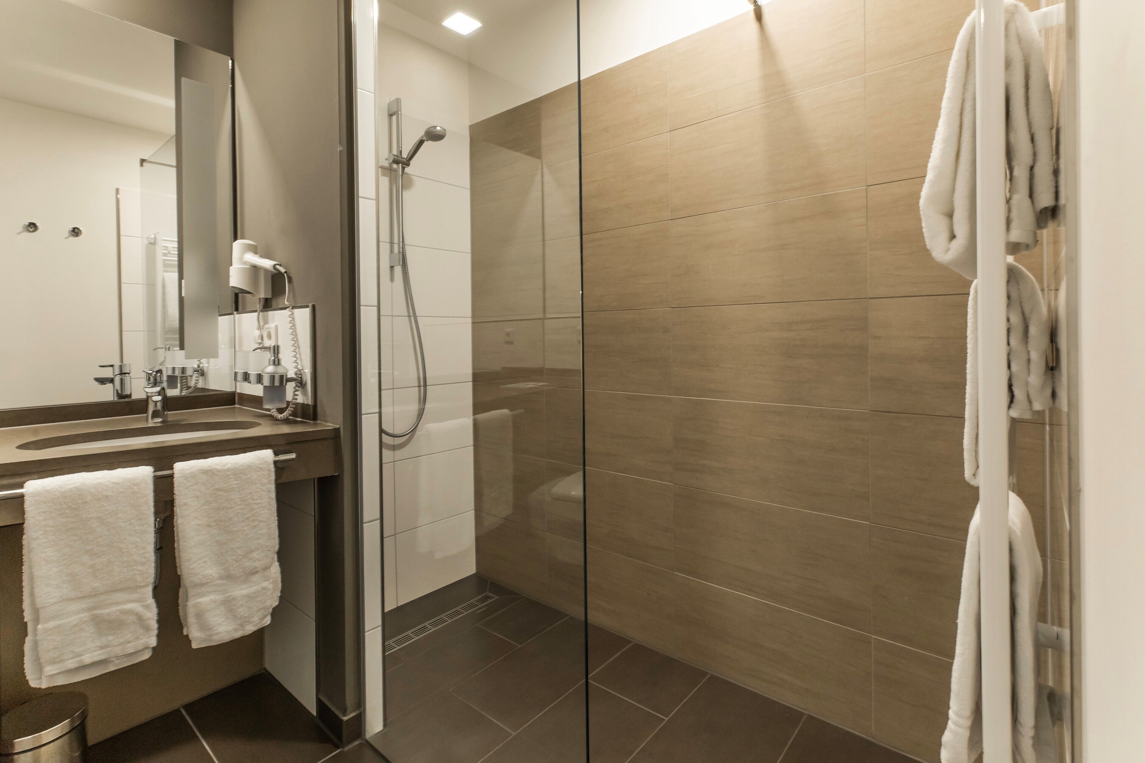 Une salle de bain moderne avec une douche à parois de verre, un lavabo équipé d’un sèche-cheveux et des serviettes accrochées au mur.