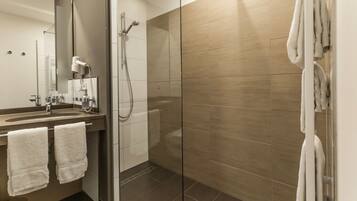 Une salle de bain moderne avec une douche à parois de verre, un lavabo équipé d’un sèche-cheveux et des serviettes accrochées au mur.