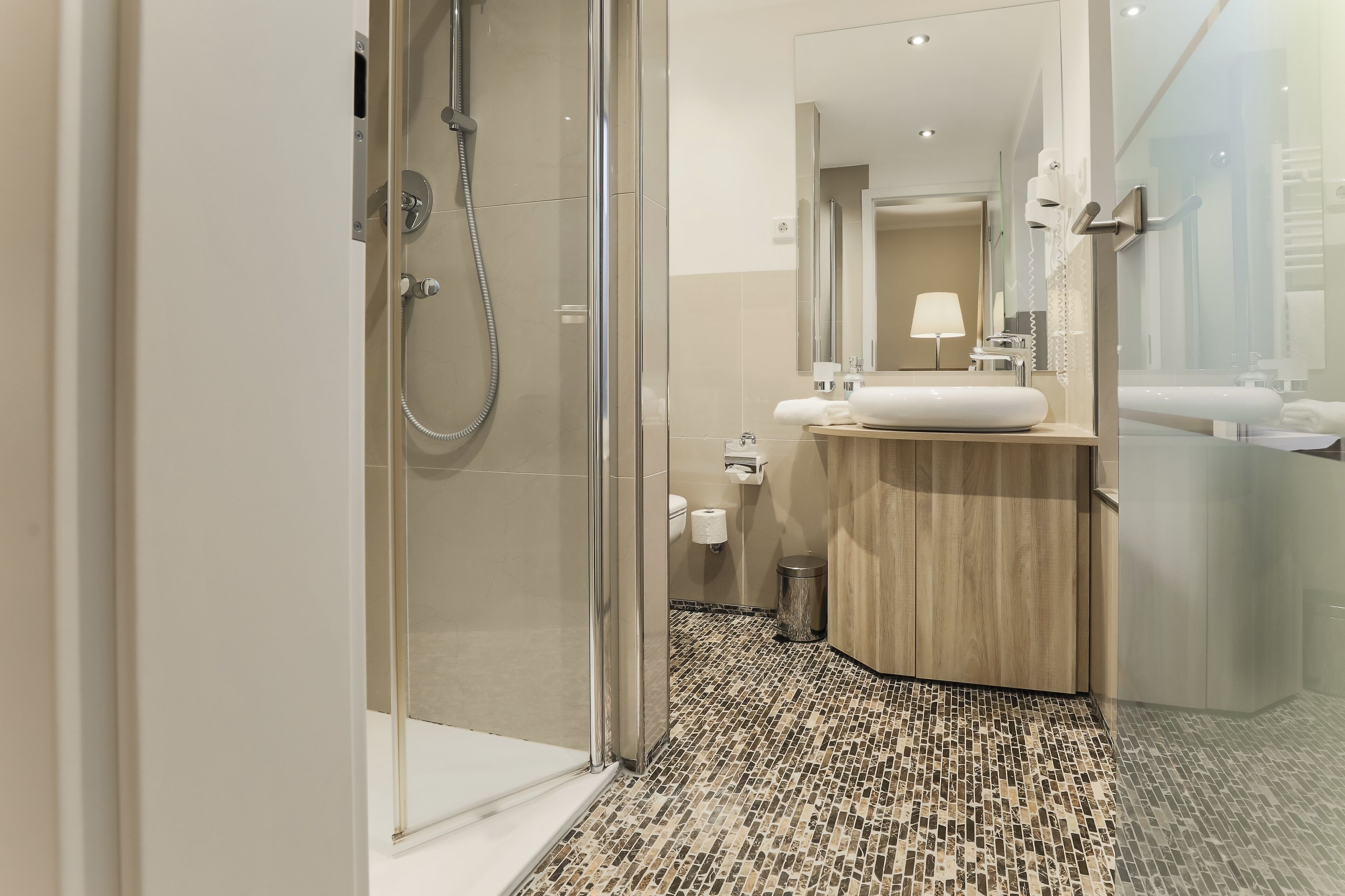 A modern bathroom with a glass-enclosed shower, a sink with a wooden vanity, and a tiled floor.