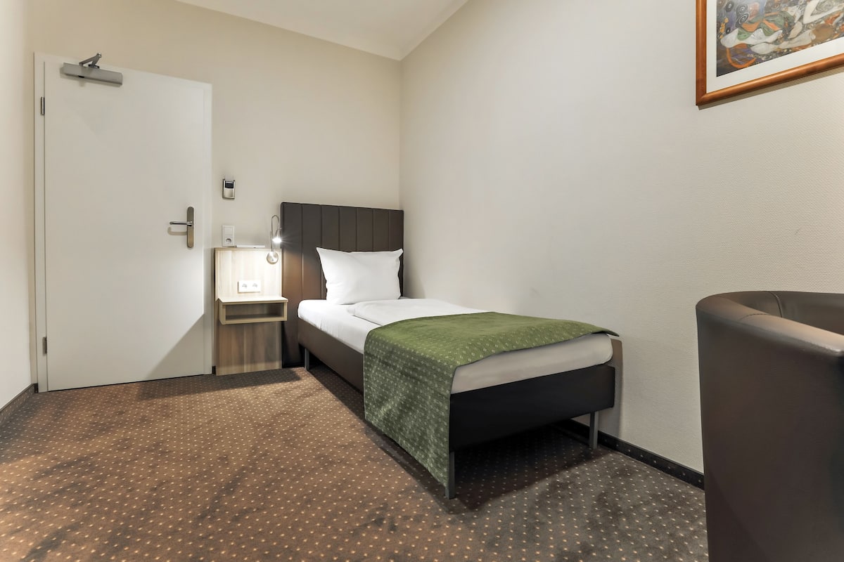 A hotel room with a bed, bedside table, lamp, and a chair.