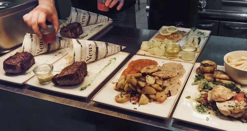 Diverse gerechten op een tafel, waaronder steak, geroosterde aardappelen en groenten.