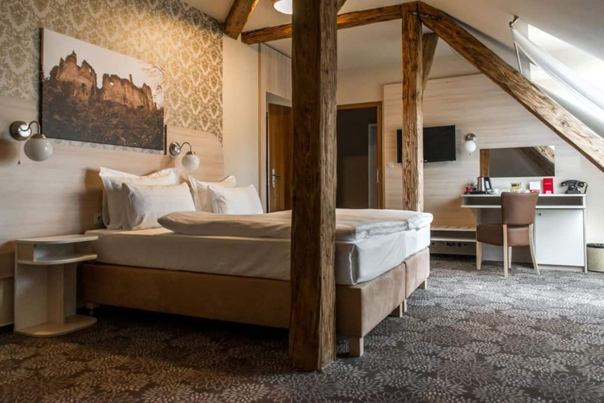 Une chambre à coucher avec un lit, des poutres en bois, un bureau et une chaise.