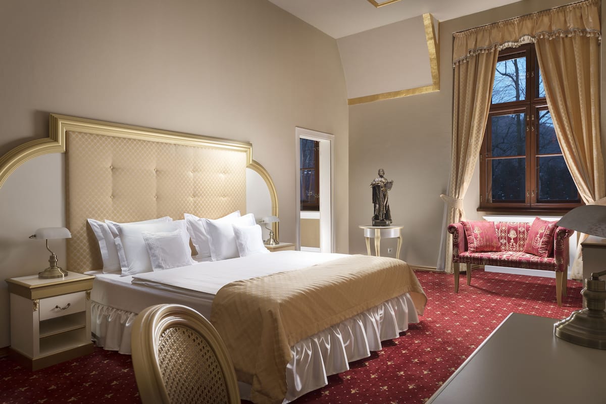 Une chambre bien rangée, avec un grand lit, des tables de chevet, une chaise et une fenêtre avec des rideaux.