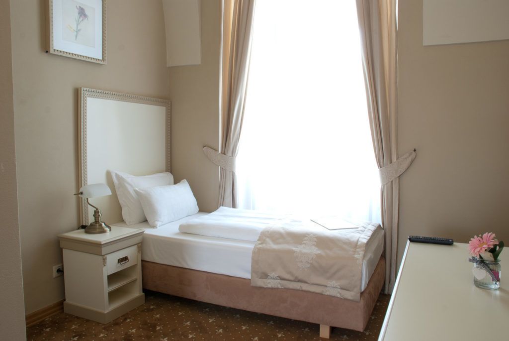 A neatly arranged bedroom with a bed, bedside table, lamp, and a small vase with flowers.