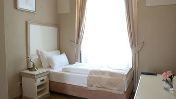 A neatly arranged bedroom with a bed, bedside table, lamp, and a small vase with flowers.