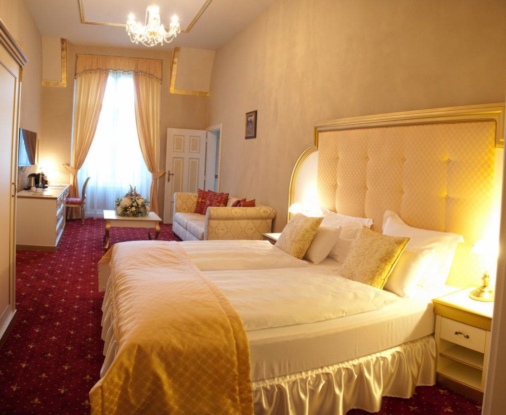Habitación de hotel con dos camas, un candelabro, un escritorio con lámpara y una alfombra roja.