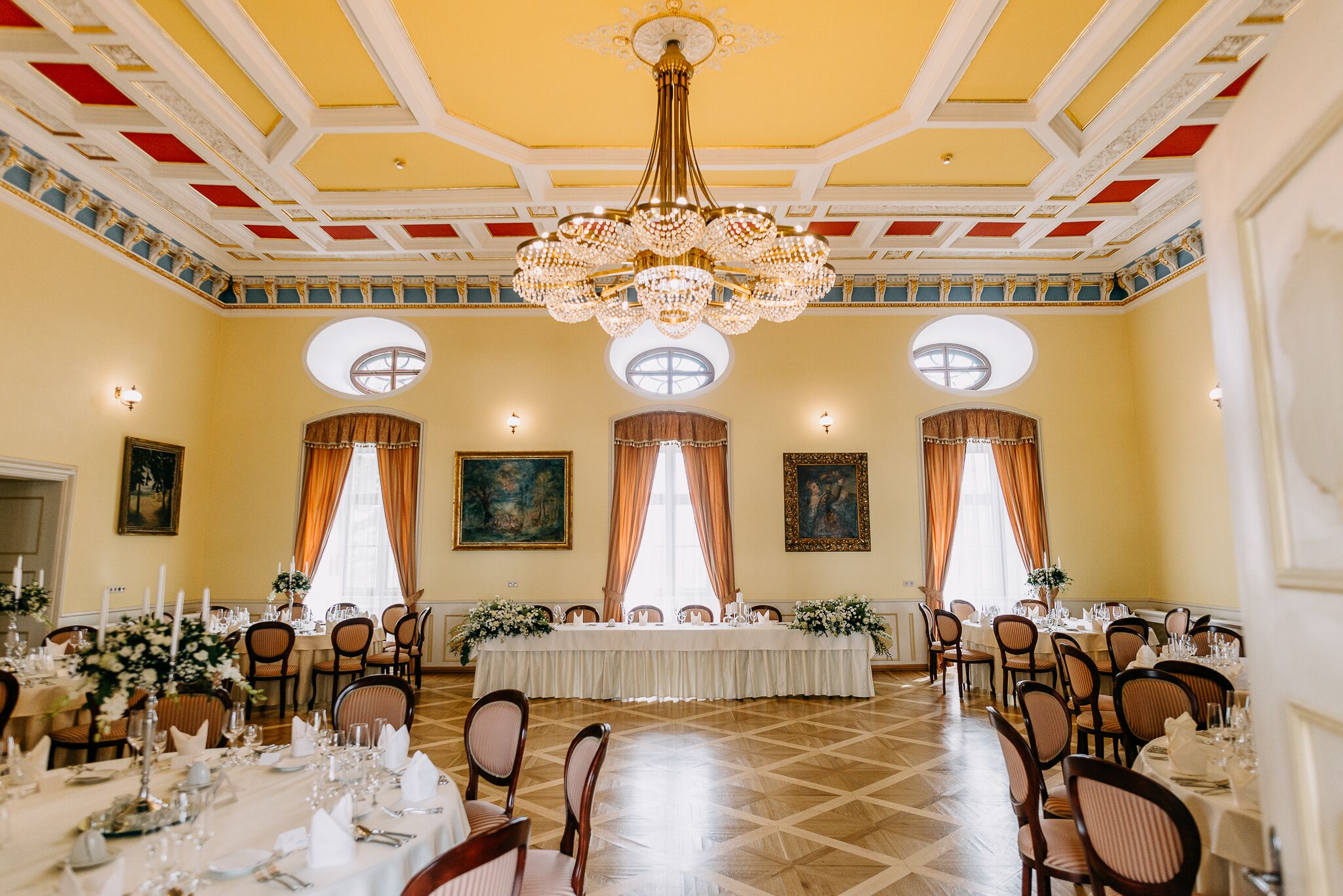 Een feestzaal met een hoge plafond, kroonluchters en een lange tafel gedekt voor een formeel evenement.