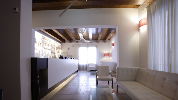 Un soggiorno moderno con un divano, una poltrona e un tavolino in vetro. Si intravede una zona cucina sullo sfondo, con una finestra e una lampada rossa.