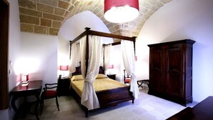 Un letto a baldacchino con tende bianche, un armadietto in legno e un soffitto in pietra.