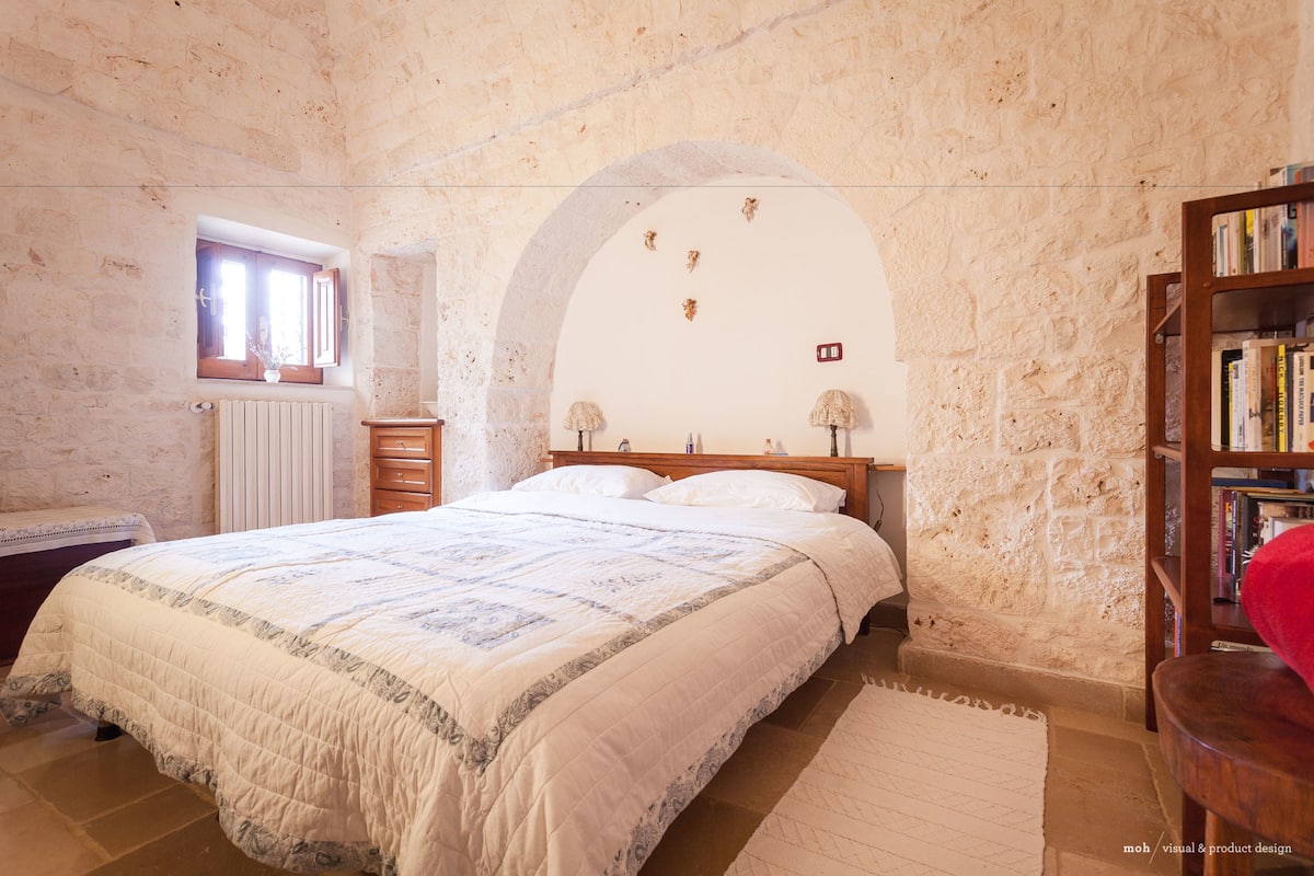 A bedroom with a large bed, a wooden headboard, a bookshelf, and a window with a view of the outside.