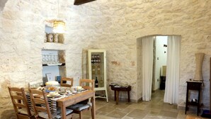 Un'area pranzo rustica con parete in pietra, tavolo e sedie in legno. Si notano un mobiletto per vini e un tavolino con riviste.