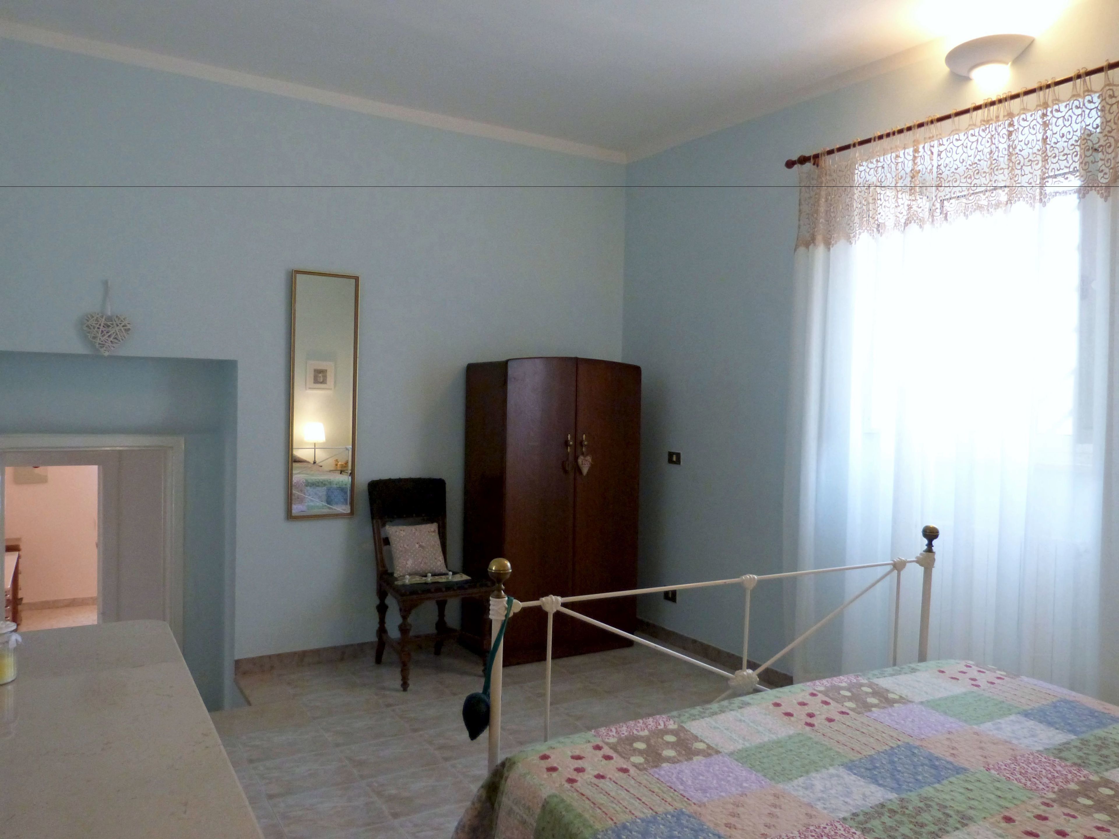 Un dormitorio con una cama, un armario de madera, una silla, un escritorio y un espejo.