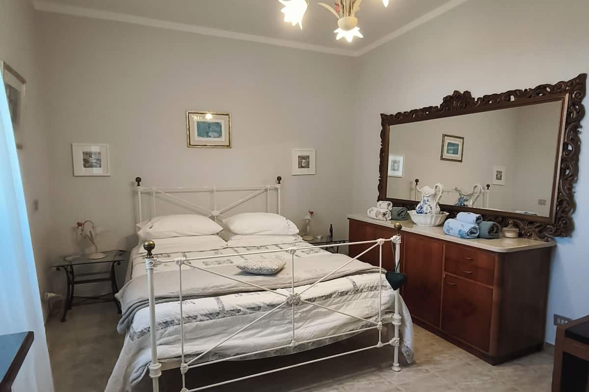 A bedroom with a bed, dresser, mirror, and wall-mounted pictures.
