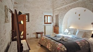 Una camera da letto con parete in mattoni, un letto con biancheria da letto floreale, un comodino in legno e una scrivania con una lampada.