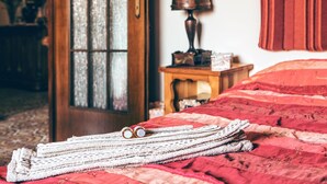 Ein ordentlich bezogenes Bett mit einer roten Tagesdecke und einem Stapel weißer Handtücher auf dem Boden.