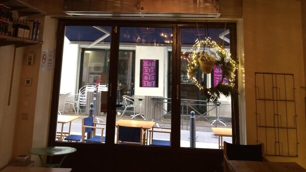 A restaurant interior with wicker pendant lighting, a view of the street outside, and a Christmas wreath on the door. - B&B La Petite Maison (Marseille)