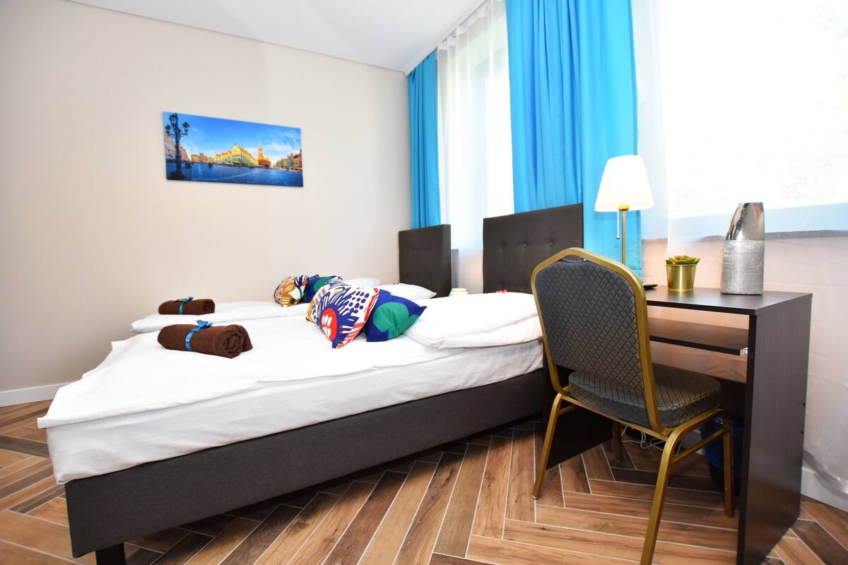 A hotel room with a bed, a desk, a chair, a lamp, and a painting on the wall.
