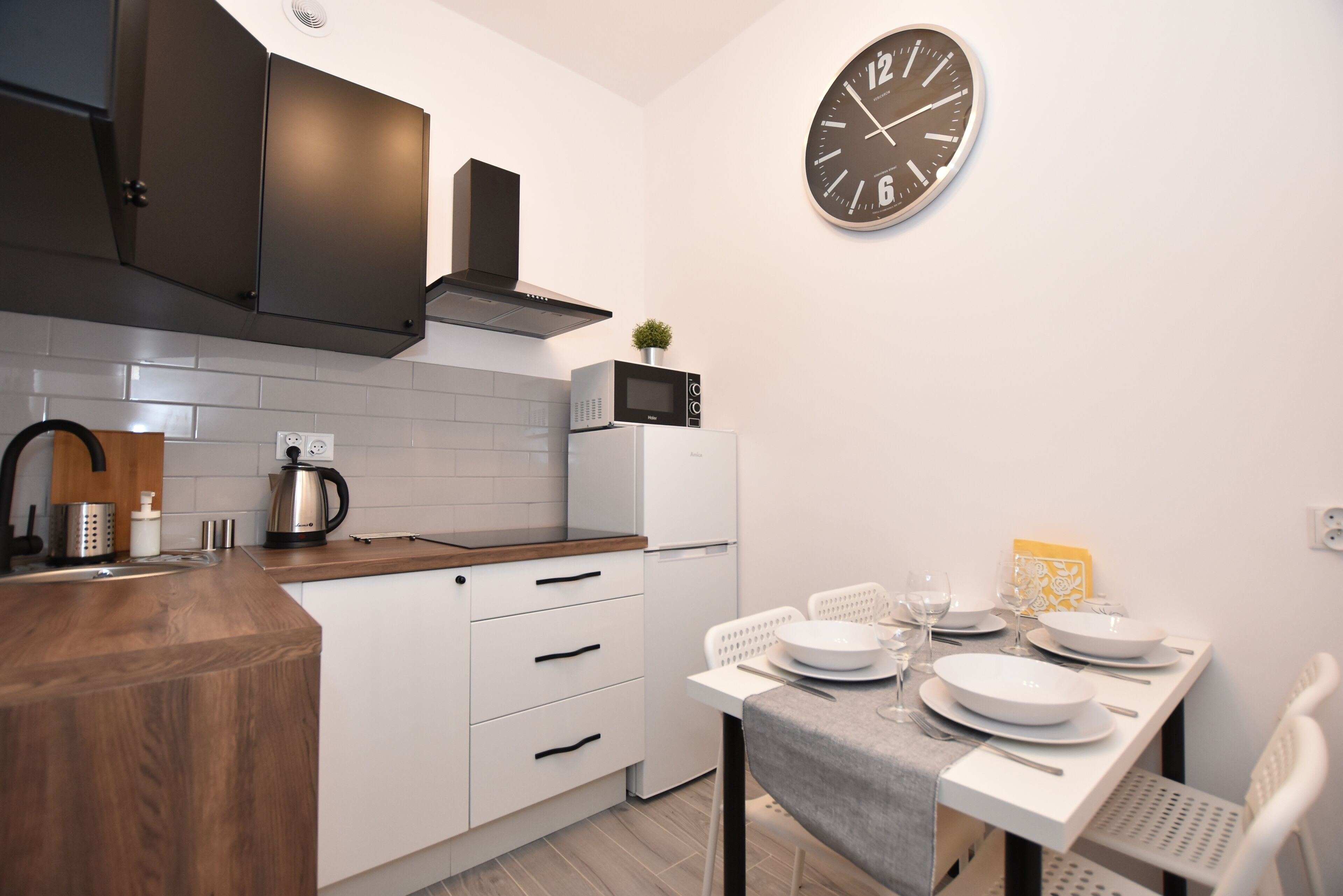 Una cocina moderna con armarios blancos, encimera de madera, microondas y un reloj en la pared.