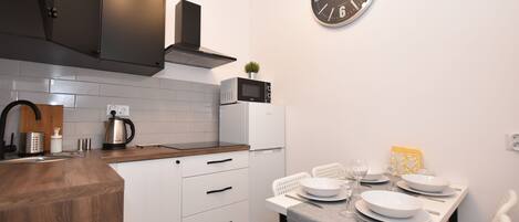 Una cocina moderna con armarios blancos, encimera de madera, microondas y un reloj en la pared.