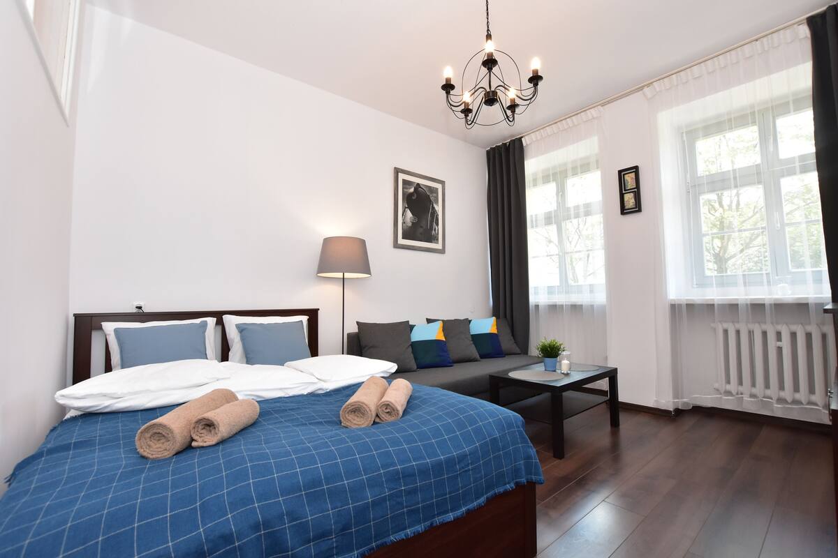 A hotel room with a bed, a sofa, a lamp, a table, and a window with curtains.