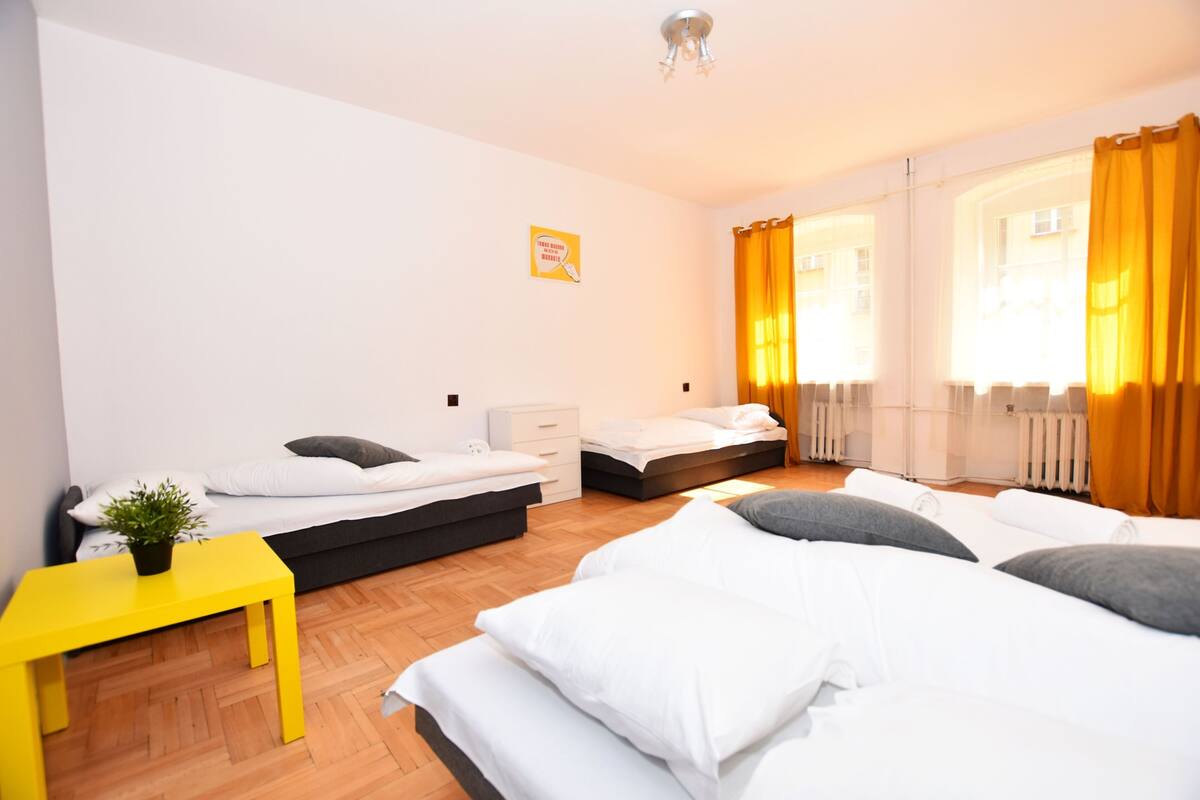 A modern bedroom with two beds, a small table with a plant, and a window with curtains.