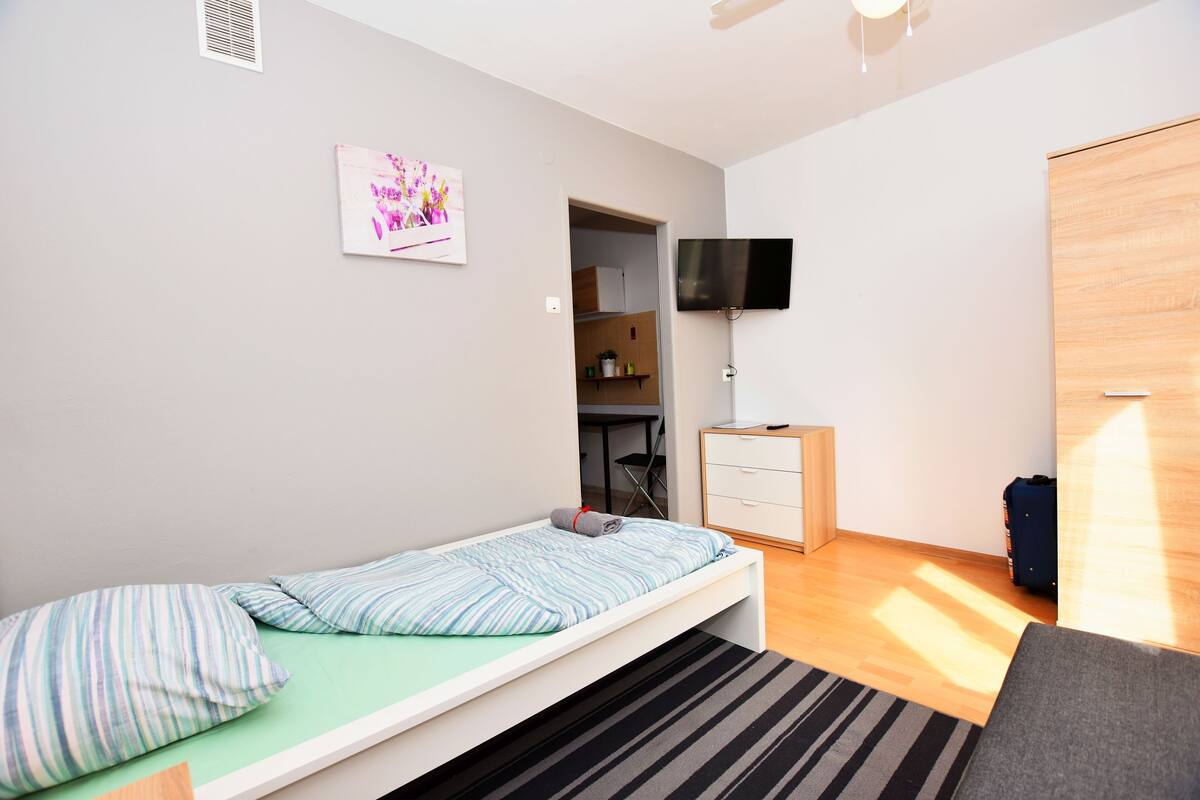 A small, modern room with a single bed, a television, a wardrobe, and a small desk.