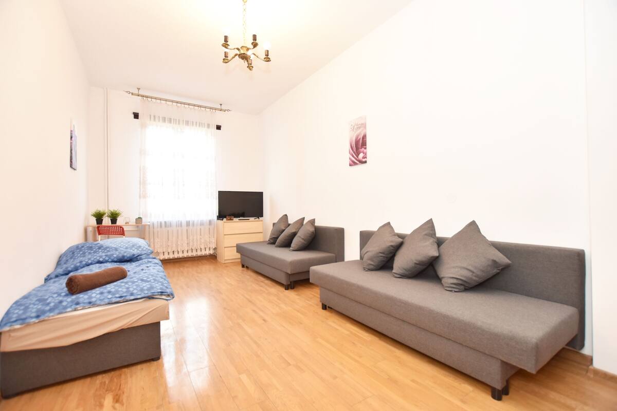 A modern living room with a sofa, a bed, a TV, and a chandelier.
