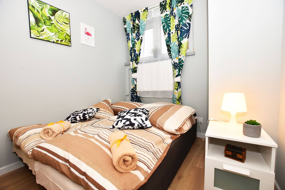 A neatly made bed with striped bedding, a bedside lamp, and a small plant on a nightstand.