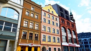 Une rangée de bâtiments aux couleurs vives, avec différentes devantures de magasins, dont un restaurant et un magasin Rossmann.