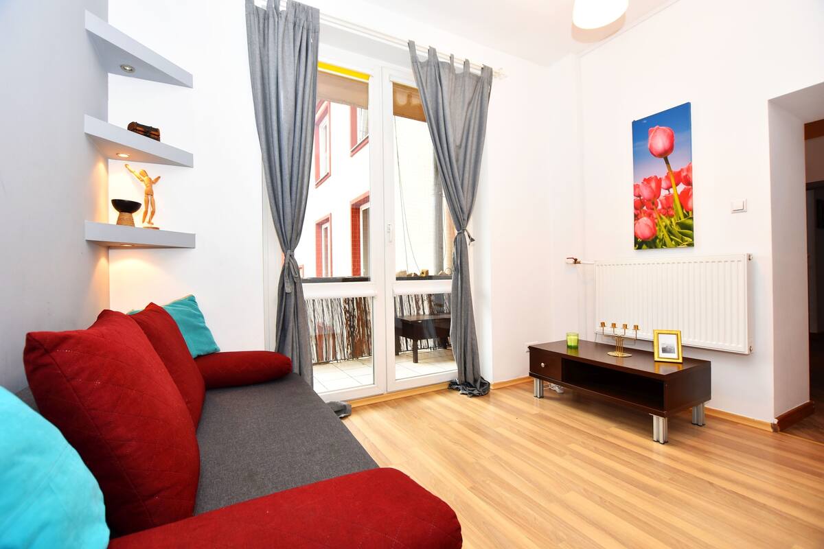 A modern living room with a red sofa, grey cushions, a wooden coffee table, and a painting of flowers on the wall.