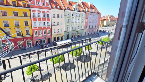 Vue sur des bâtiments aux couleurs vives et une place publique, prise depuis un balcon.