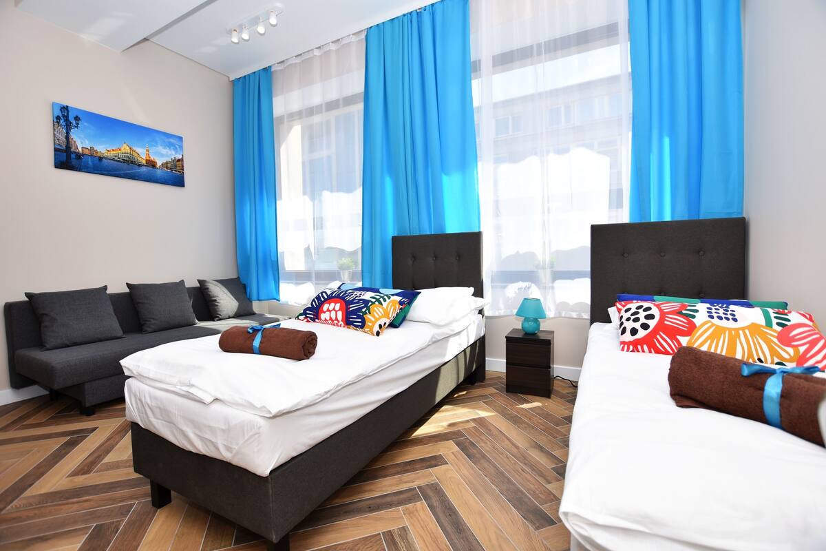 A hotel room with two beds, a sofa, a nightstand, and a painting on the wall.